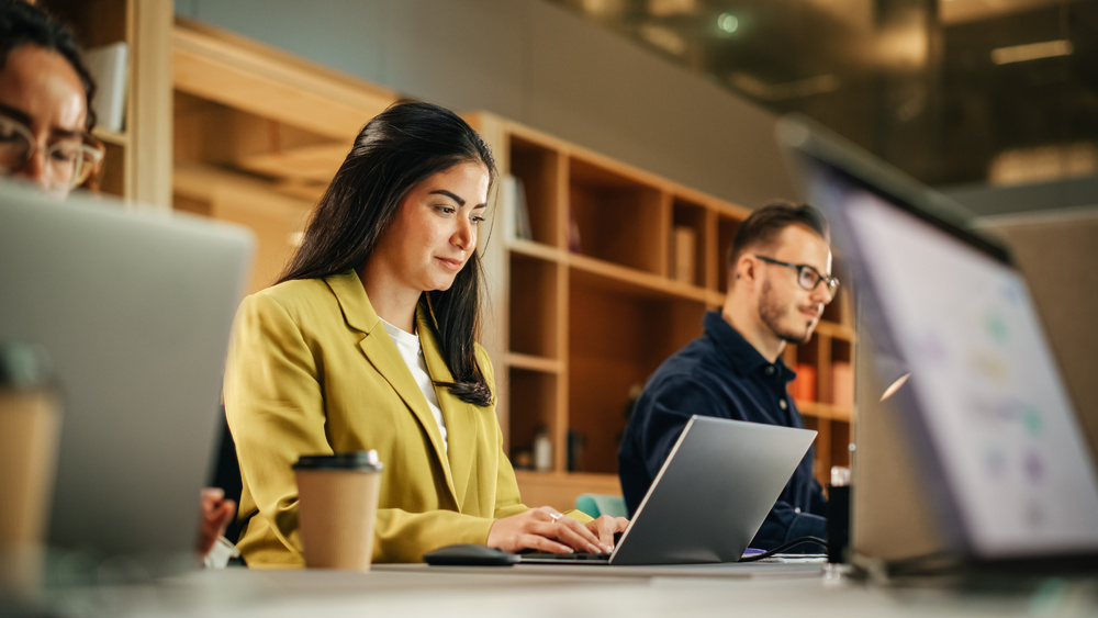 A female employee works on a laptop beside two male co-workers. 