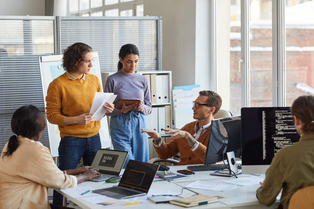 An IT development team meeting in an office with large windows.