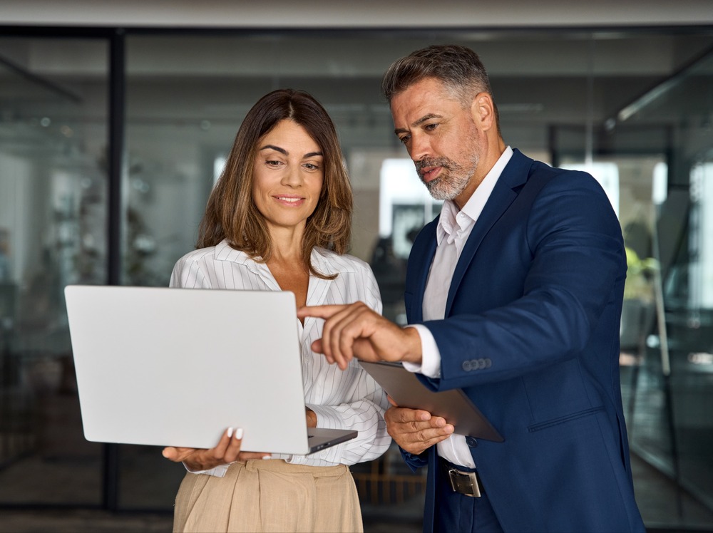 Two business people review information on a laptop in an office. 
