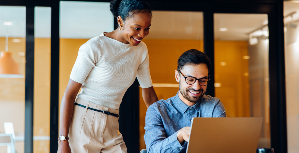 Two colleagues review organizational goals together using a laptop in a modern office.